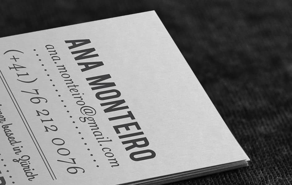 Close-up of the business card’s corner: “Ana Monteiro” in bold condensed capitals beside her email in script and her phone number in a light typewriter face